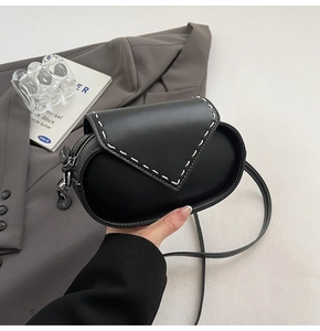 Detail view of a black oval crossbody bag featuring white contrast stitching and silver hardware