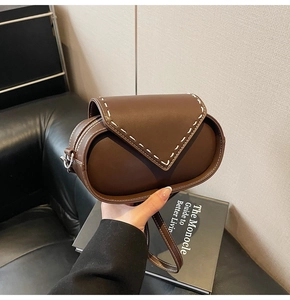 Detail of a brown leather shoulder bag featuring bold white contrast stitching and silver hardware
