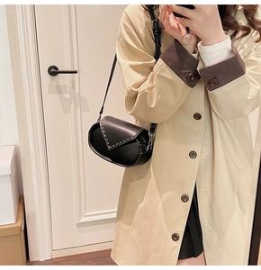 Detail of black leather saddle bag with white contrast stitching on khaki trench coat