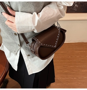 Close-up of a vintage brown saddle bag featuring white contrast stitching and smooth leather