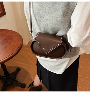 Brown vintage leather crossbody bag with white contrast stitching in a cozy cafe setting