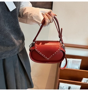 Detail of red oval leather bag featuring contrast white stitching and metal buckle