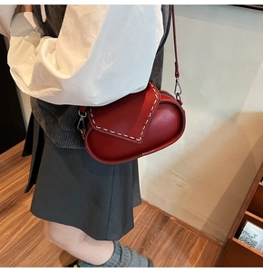 Detail of red leather crossbody bag featuring distinctive white hand-stitched decorative seams