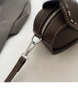 Detail of silver hardware and white contrast stitching on dark brown leather crossbody bag