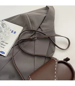 Detail of adjustable strap and white stitching on dark brown leather crossbody bag
