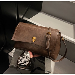Détail de la texture cuir craquelé marron foncé vintage et fermoir métallique doré du sac