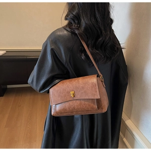 Détail d'un sac à bandoulière marron vintage avec fermoir doré porté à l'épaule