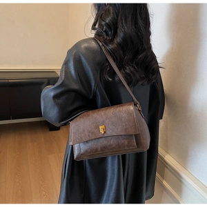 Détail du sac bandoulière vintage marron foncé avec texture rétro et boucle dorée sur modèle