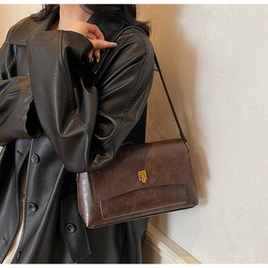 Détail du sac bandoulière vintage en cuir marron foncé avec boucle dorée sur veste noire
