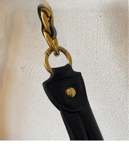 Close-up of black leather shoulder strap with luxury gold metal rings and chain detail