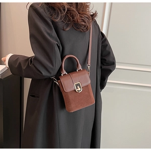 Close-up of brown suede crossbody bag with gold metallic clasp and smooth leather handle