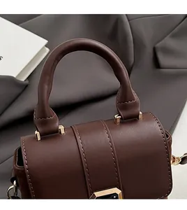 Detail of dark brown leather handbag featuring a smooth curved handle and gold metal buckles