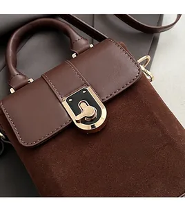 Close-up of golden metal clasp on dark brown suede and leather crossbody bag detail