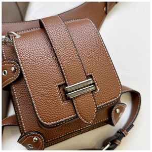 Close-up of brown lychee grain leather crossbody bag with white stitching and metal buckle