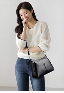 Close-up of black litchi leather shoulder bag with decorative silver leaf metal buckle