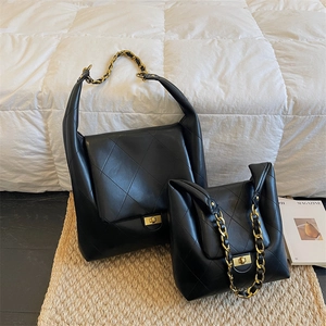 Black quilted crossbody bag with gold chain strap in two sizes on white bedding
