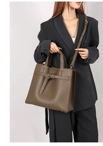 Brown-green lychee leather tote bag with decorative buckle shown on shoulder of model