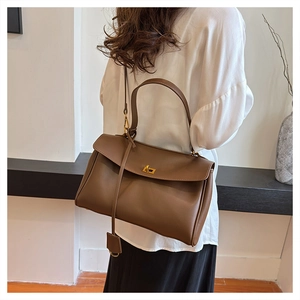 Brown leather tote bag featuring a gold twist lock and adjustable shoulder strap worn by model
