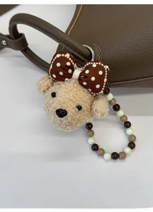 Détail d'un charme d'ours en peluche avec nœud à pois et lanière perlée sur un sac à main