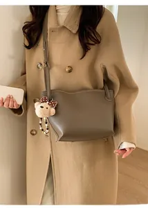 Détail d'un sac seau gris-brun avec breloque ours porté sur un manteau en laine camel