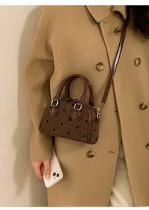 Mini brown polka dot Boston bag with leather trim worn on a camel coat by a model