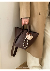 Gros plan sur un sac seau marron foncé à texture litchi avec un charmant pendentif