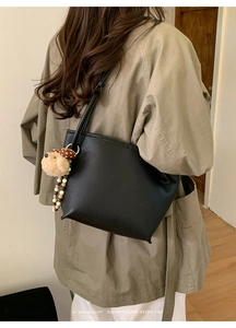Détail du sac à main noir en cuir grainé avec breloque d'ours sur mannequin en manteau kaki