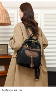 Detail of black pebbled leather backpack with brown trim and long tassel zippers on a model