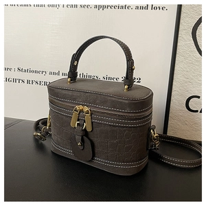Detail of dark brown faux crocodile leather bag with contrast stitching and gold zipper