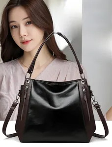 Detail view of contrast brown handles and polished black leather panels on the tote bag