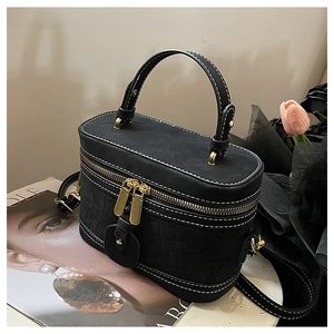 Detail of black vanity bag with crocodile texture, gold zippers and white contrast stitching