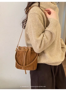 Detail of caramel brown tassel bucket bag with drawstring closure and metal ring accents
