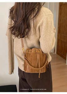 Brown suede bucket bag with fringe detail shown on shoulder of model in casual setting