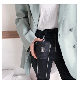 Detail of black shimmer cylinder mini bag with silver lock worn by model in green suit