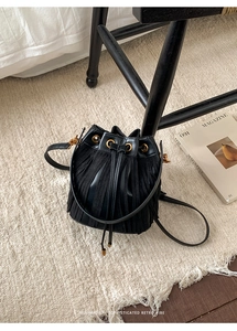 Detail of black drawstring bucket bag featuring long fringe tassels and golden hardware