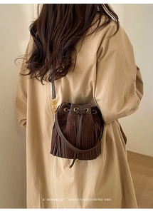Detail of dark brown suede bucket bag featuring chic fringe and gold metallic buckles