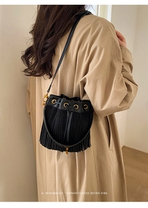 Detail of a vintage black tassel bucket bag worn over a beige trench coat