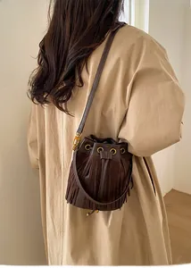 Detailed view of dark brown fringe bucket bag worn with a beige trench coat