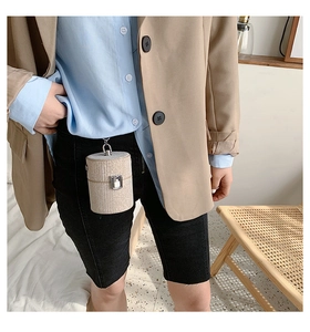 Mini cylindrical woven bag with silver metal handle clipped onto black denim shorts