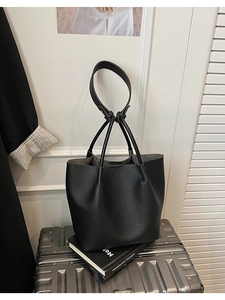 Close-up of black lychee grain tote bag with knot shoulder strap on silver suitcase