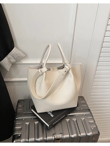 Detail of off-white lychee grain leather bucket bag on minimalist luggage setup