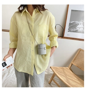 Detail of a light yellow linen shirt and a silver cylindrical chain bag on a model
