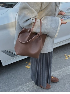 Brown lychee grain leather bucket bag shown in a professional lifestyle autumn commute setting