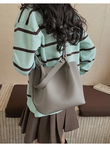 Detail showing the gray pebble leather bucket bag worn by a model in a casual outfit