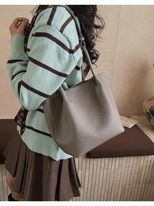 Litchi texture grey leather bucket bag worn by a model in a minimalist indoor setting
