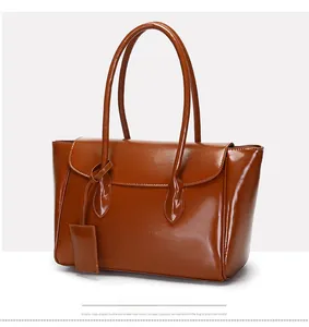 Detail of a brown glossy patent leather tote bag with elegant handles and decorative tag
