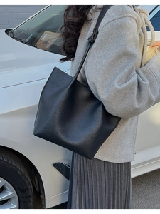 Close-up of black lychee grain leather tote bag worn as a shoulder bag in outdoor setting