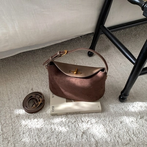 Retro brown suede crossbody dumpling bag with gold twist lock on a white magazine