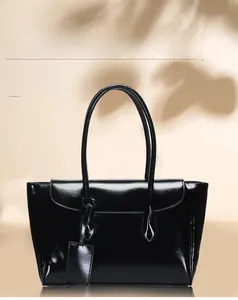 Close-up of glossy black tote bag with slender handles and hanging charm detail