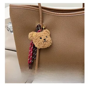 Detail of brown teddy bear plush charm with woven rope accents on a leather tote bag